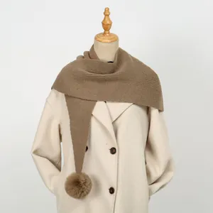 Dicker Strickschal mit Kunstfell-Pompons auf einem weißen zweireihigen Mantel präsentiert