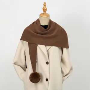 Detail eines dunkelbraunen Strickschals mit Bommeln auf elfenbeinfarbenem Wollmantel