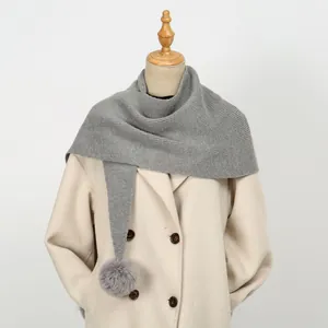 Detail eines grauen Strickschals mit Pompons gestylt auf einem beigen zweireihigen Mantel