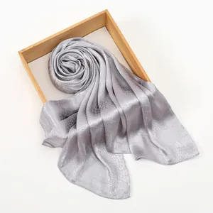 Detail of silver grey scarf with glossy snake skin texture on a wooden tray