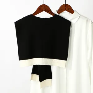 Detail of black knit shawl with wide white ribbed hem draped over a white collared shirt