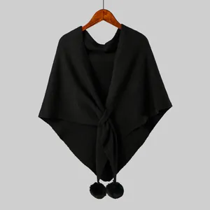 Detail of black knit shawl with a cross-knot design and faux fur pom-pom trim on wood hanger