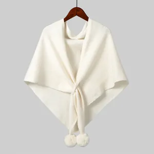 Detailed texture of beige knit shawl featuring pom-pom charms and crossover design