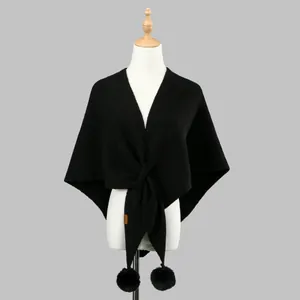 Close-up of black knitted shawl with soft pom-poms and leather brand label detail