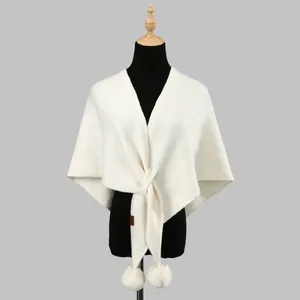 Detail of cream knit shawl with decorative fur pom-poms and front knot design