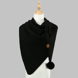 Detail of black knit triangle shawl featuring a soft pompom and leather brand label