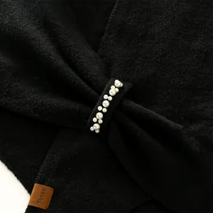 Detailed view of black textured shawl with elegant pearl accents and leather label