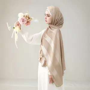 Close-up of light beige chiffon hijab with fine stripes texture held by a model