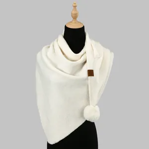 Detail of cream knit shawl featuring a soft pom-pom and leather logo tag texture