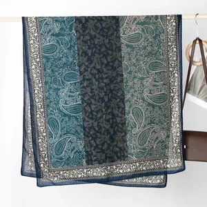 Detail eines blauen Paisley-Leinenschals an einem Holzgestell mit Lederhandtasche