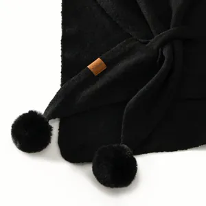 Solid black knit shawl with fluffy pom-poms and minimalist leather label accent