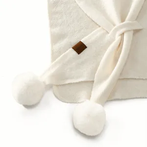 Detail of soft cream knitted shawl texture with fluffy pom-poms and leather logo tag