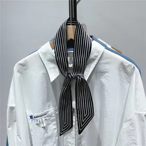 Detail of a white cotton shirt featuring a black striped neck scarf and blue brand label
