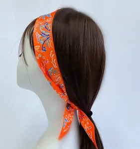 Macro shot of orange silk-like skinny scarf tied as a headband with pop-art paisley pattern