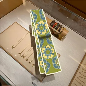 Luxurious sage green twilly silk scarf with floral patterns on a jewelry counter display