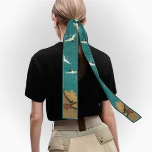 Detailed texture of green silk ribbon scarf with crane print tied on low ponytail