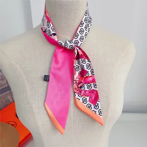 Detail of a narrow silk-like scarf with vibrant pink and orange geometric letter patterns