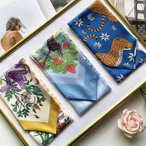 Three elegant narrow silk scarves with floral, tiger, and leopard prints on a white tray