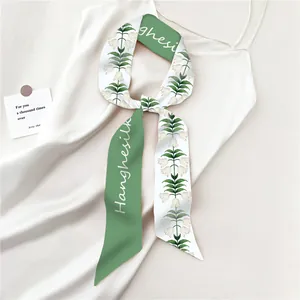 Detail van een zijden sjaal geknoopt op een witte jurk met groen lelietje-van-dalen