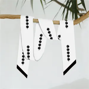 Detail van witte smalle twilly sjaal met zwarte kralenpatronen op een houten tak