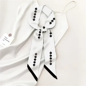 Detailopname van een witte zijden sjaal met minimalistische zwarte parelprint op jurk