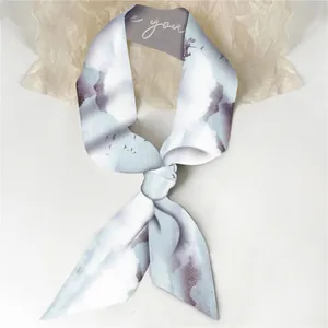 Detail van een blauwe zijden sjaal met inktlandschapspatroon en elegante geknoopte styling