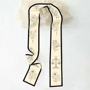 Detail van de crème twilly sjaal met botanische print en zwarte smalle rand