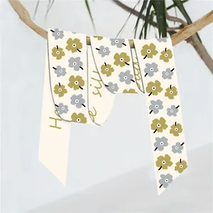 Detail van een smalle zijden sjaal met bloemenprint en gouden tekst aan een tak