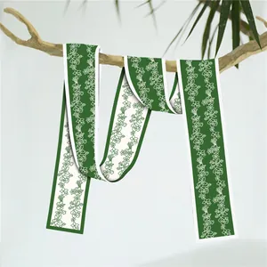 Detail van groene smalle zijden sjaal met bloemenpatroon hangend aan een tak