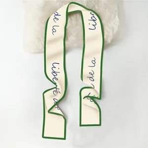 Detail van een elegante crème twilly sjaal met groene randen en blauwe tekstprint