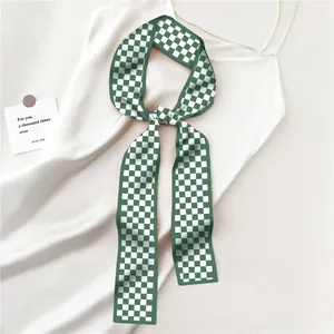 Detail van groen-witte geblokte zijden sjaal geknoopt op een witte camisole jurk