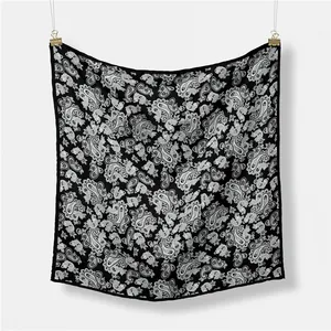 Classic black and white paisley silk scarf displayed on a textured white background