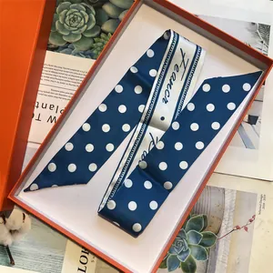 Dettaglio del foulard in seta blu navy a pois riposto in una confezione regalo arancione