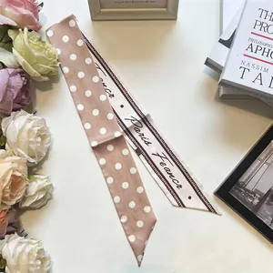 Dettaglio della sciarpa in seta a pois rosa champagne e twilly con stampa parigina