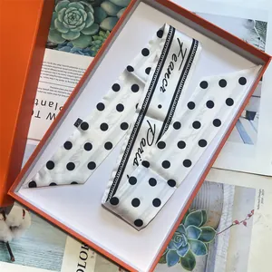 Dettaglio del foulard di seta a pois bianchi con testo Paris in un'elegante confezione arancione