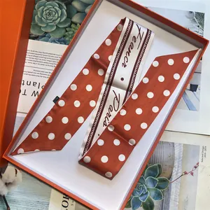 Dettaglio della sciarpa sottile a pois caramello in una confezione regalo arancione