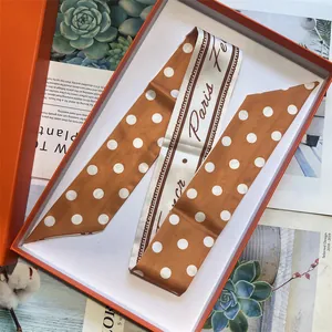 Dettaglio del foulard in seta a pois marroni e bianchi in una scatola regalo arancione