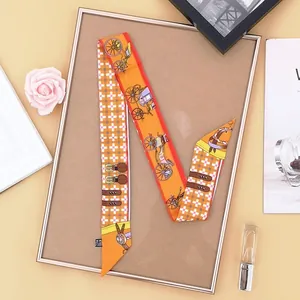 Detail view of orange silk twilly scarf with carriage pattern on a decorative background