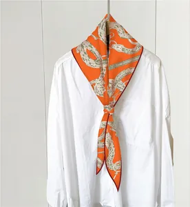 Detalle de pañuelo naranja estampado con motivo de serpiente sobre cuello de camisa blanca