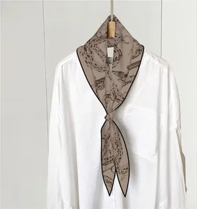 Detalle de un pañuelo twilly con estampado de serpiente y cadena en cuello de camisa