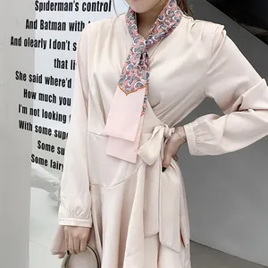 Detail of a light pink satin wrap dress featuring a paisley print silk neck scarf accessory