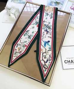 Narrow silk scarf with floral bird print and striped edges draped on a gold frame