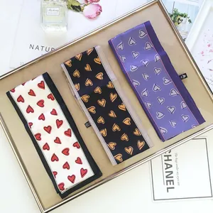 Three long silk scarves with heart patterns in white, black, and purple on a gold tray