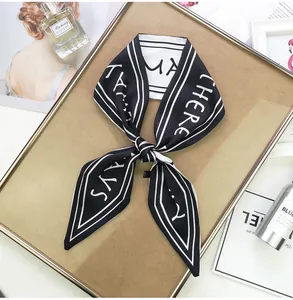 Detail of a black and white silk ribbon scarf with letter print on a wooden tray