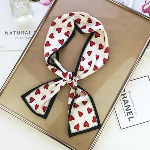 Detail of white skinny silk scarf with red heart patterns on a stylish gold frame background