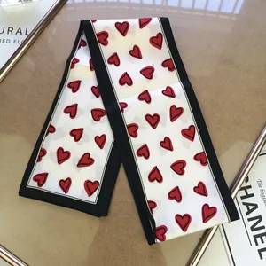 Detail of a white long silk scarf with red heart prints and black borders on decor