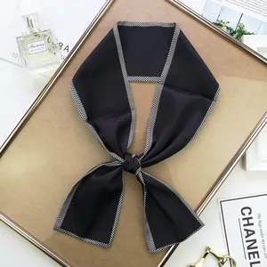Détail d'un foulard étroit en satin soyeux avec bordure à chevrons noirs et blancs
