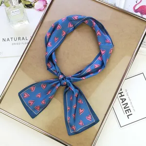 Detailed view of a long navy blue satin twilly scarf with pink hearts on a gold tray