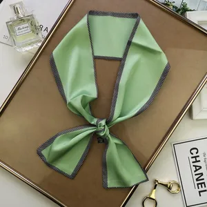 Détail d'un foulard en soie vert clair avec bordure diagonale noire et blanche élégante