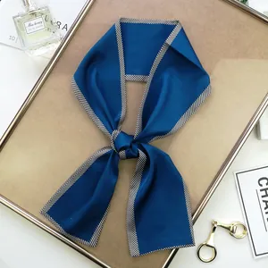 Détail d'un foulard en soie bleu marine avec bordures rayées noué en nœud élégant